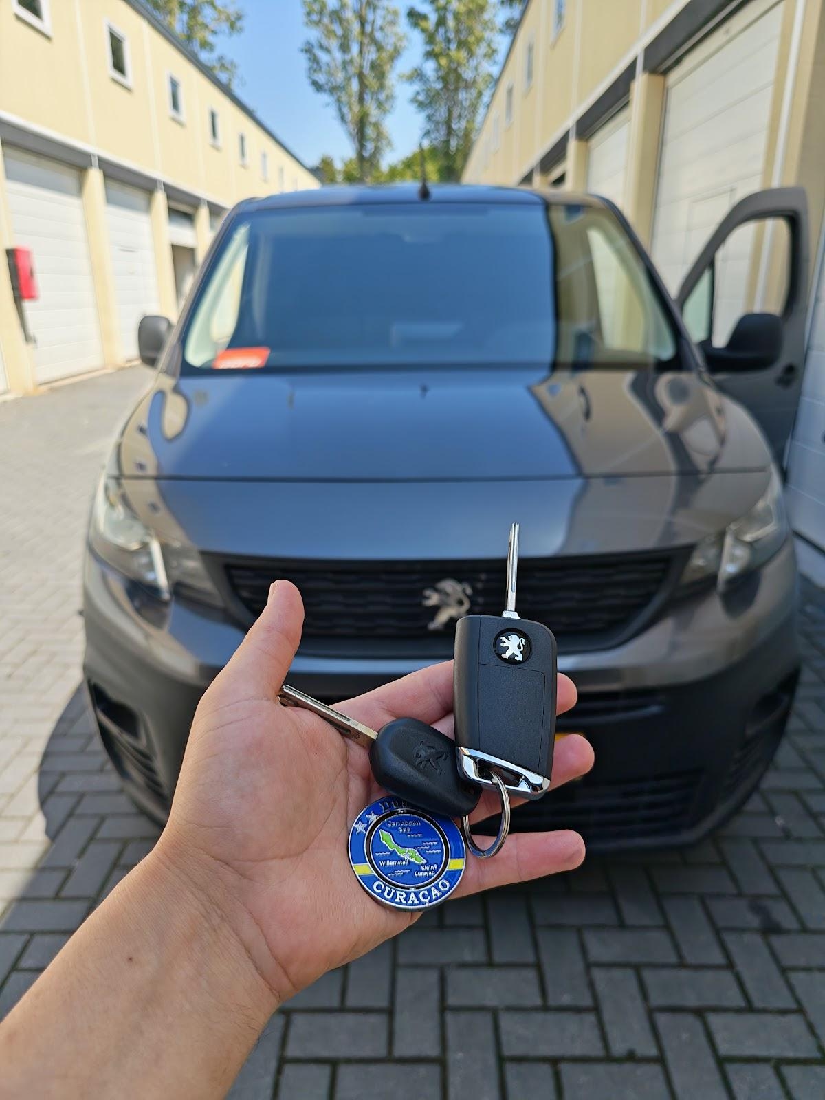 Een klapsleutel en een vaste autosleutel in de hand voor een grijze Peugeot bus