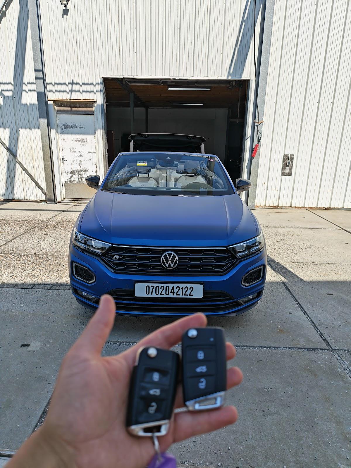 Twee autosleutels in de hand voor een blauwe Volkswagen T-Roc cabrio